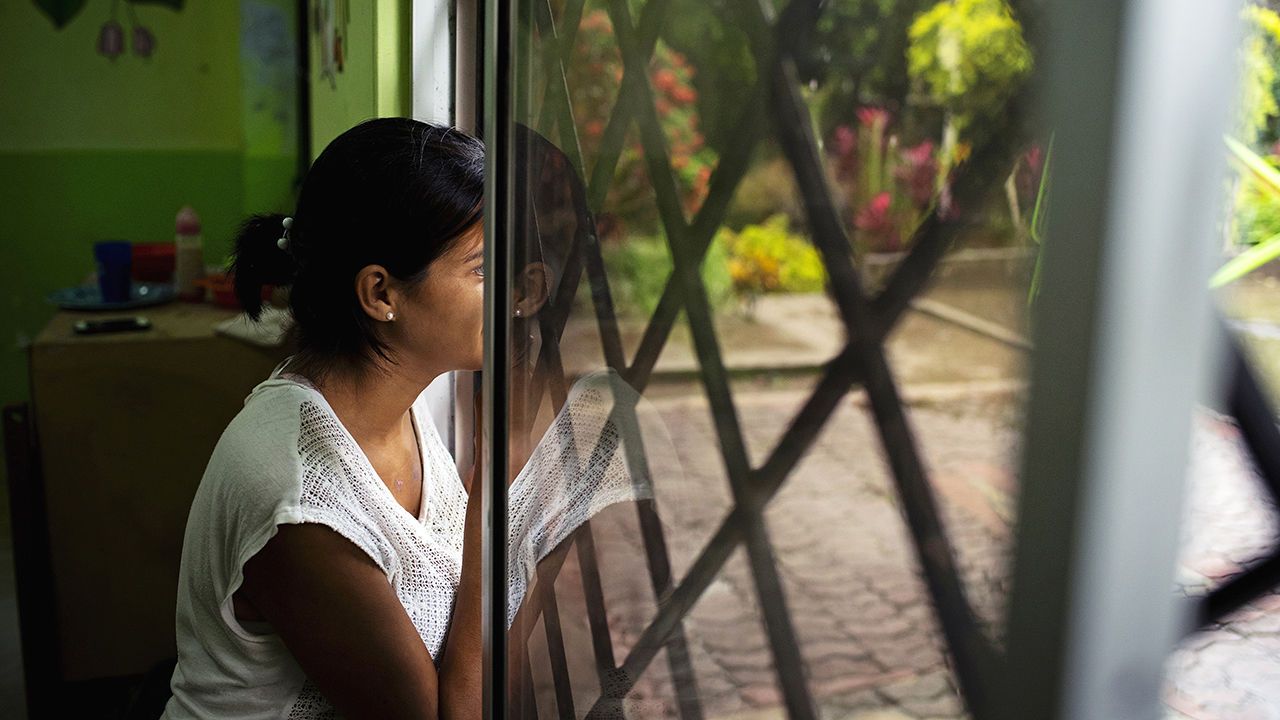 Woman looks out of a window at a shelter for women in Ecuador.